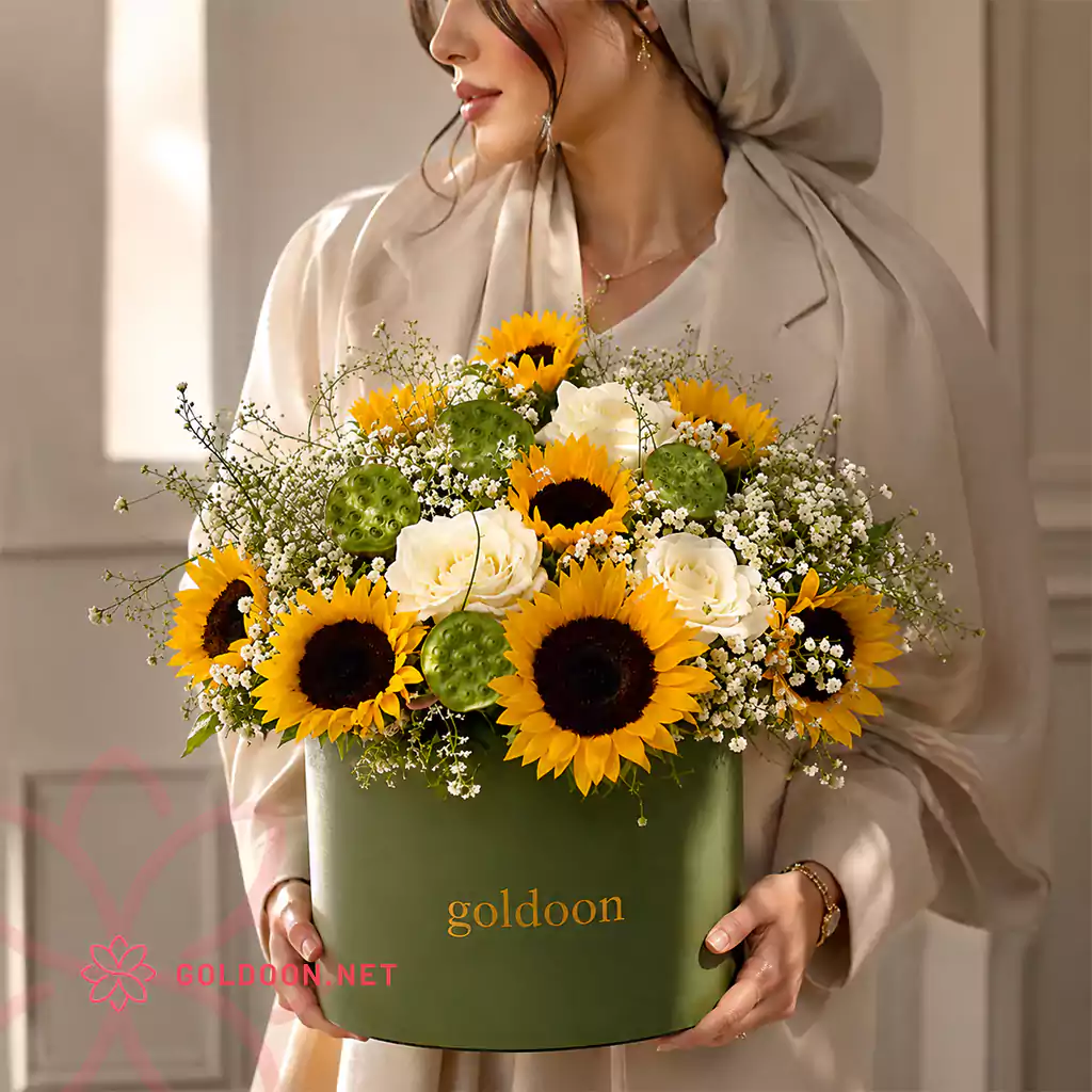 باکس گل کد 008 از گلدون؛ ترکیبی از آفتابگردان، رز سفید، ژیپسوفیلا، غلاف پسته دریایی و برگهای تزئینی در باکس استوانهای سبز؛ با ابعاد 40*40