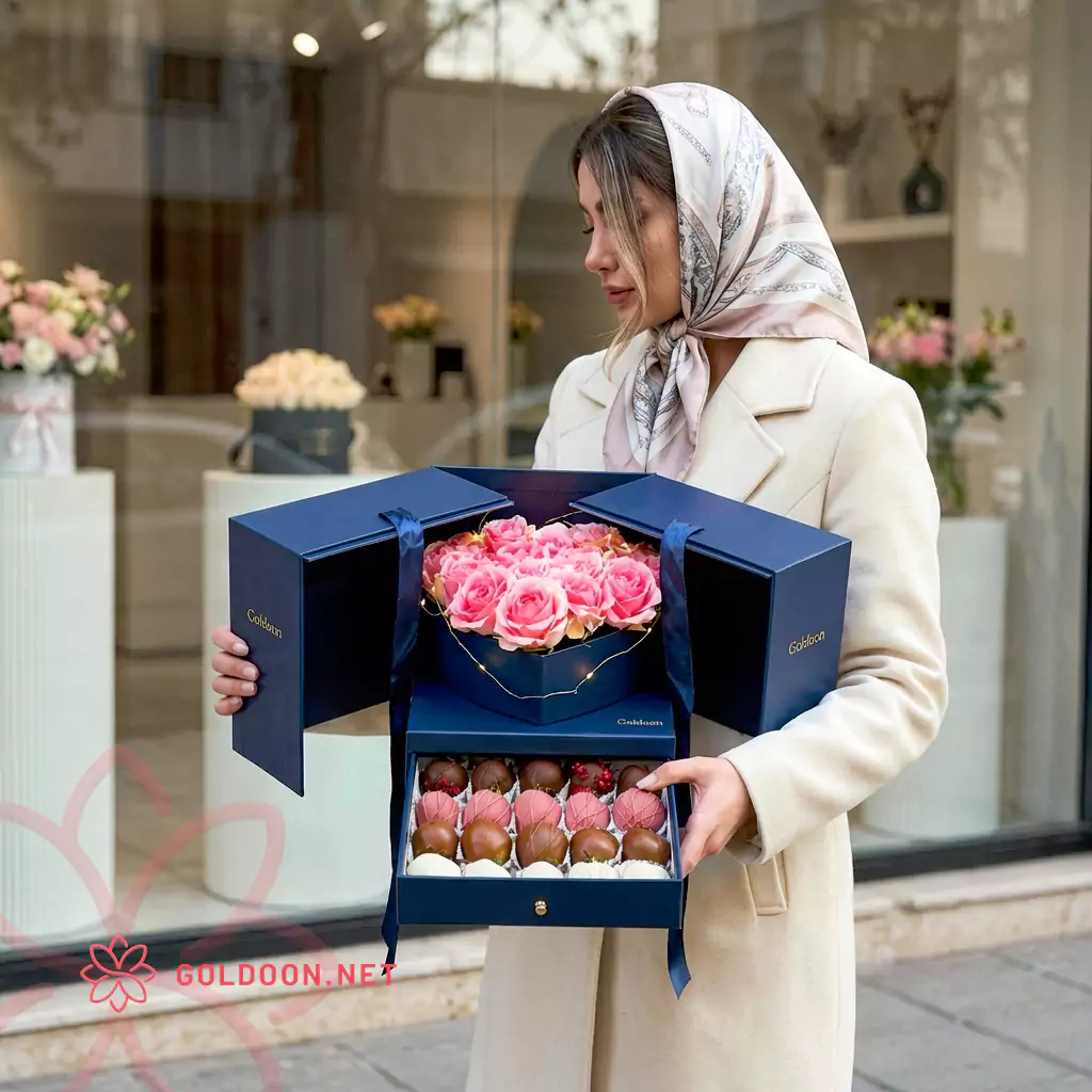 باکس هدیه گل و شکلات کد 030 از گلدون؛ ترکیبی از رزهای صورتی تازه و شکلاتهای متنوع در باکس هدیه دوطبقه سرمهای با طراحی لوکس و مدرن؛ با ابعاد 30 × 30 × 30 سانتیمتر