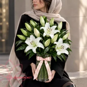 جار گل لیلیوم سفید کد 012 مدل 15 شاخه در گلدان شیشه‌ای در دستان مدل خانم
