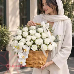 سبد گل رز سفید و ارکیده کد 003 با خزه و شاخ‌وبرگ سبز در سبد حصیری عسلی در دست مدل خانم