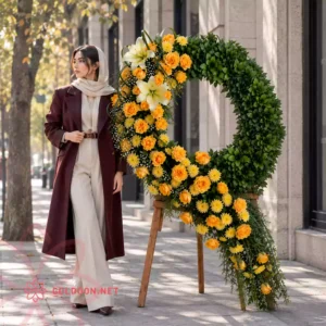 تاج گل کد 010 با رزهای زرد و نارنجی، لیلیوم روشن و برگ‌آرایی سبز در کنار مدل خانم